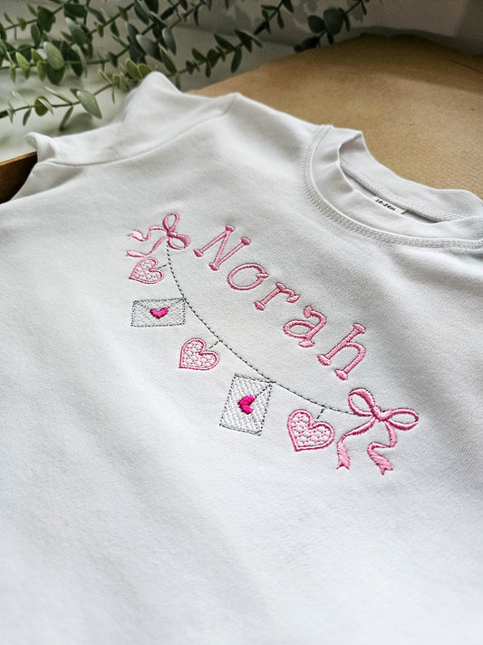 White tshirt with pink embroidery of 'Norah' and decorative valentine elements