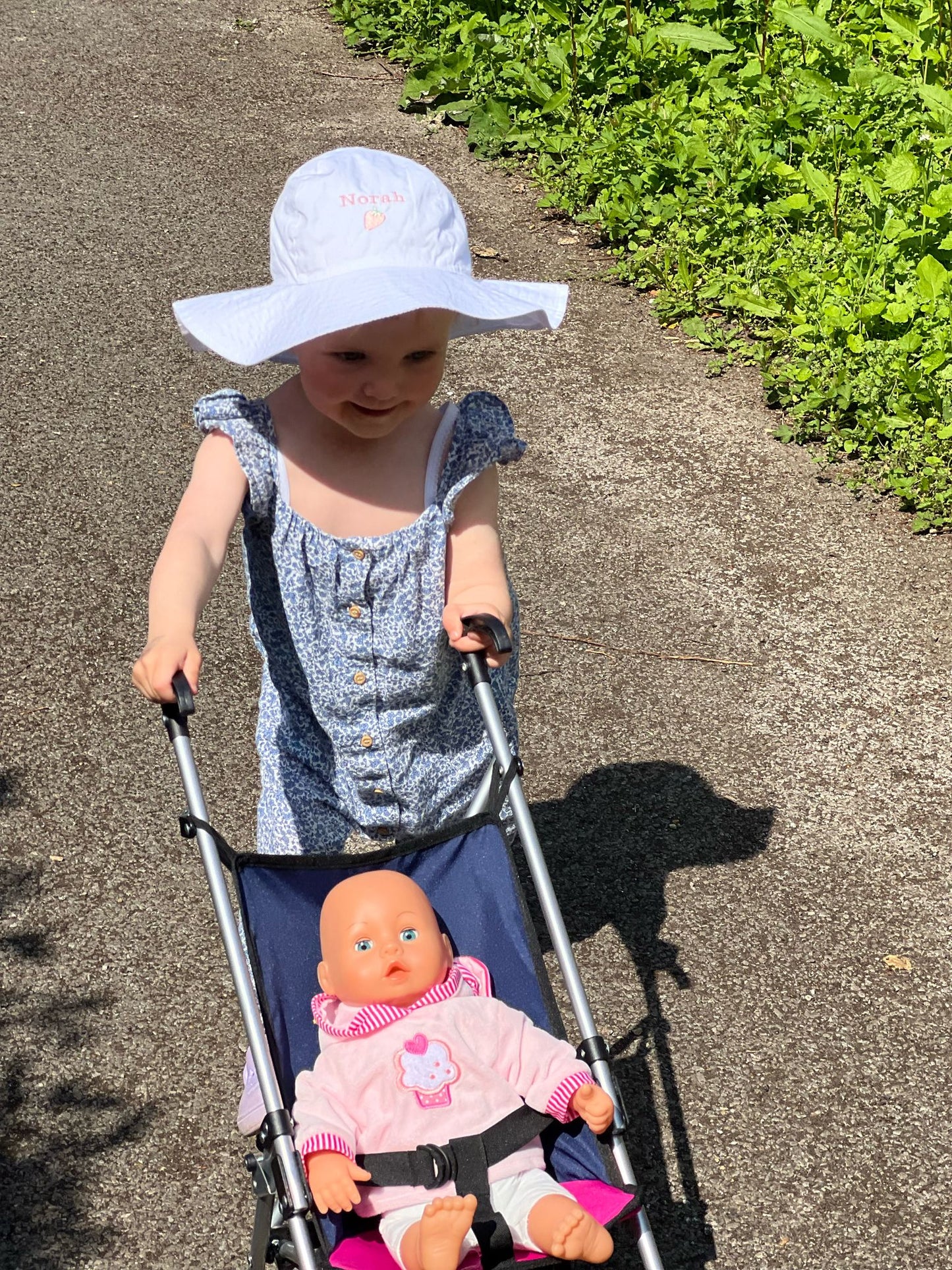 Little girl wearing white wide brimmed sun hat personalised with name and cute pink strawberry design embroidered on the front.