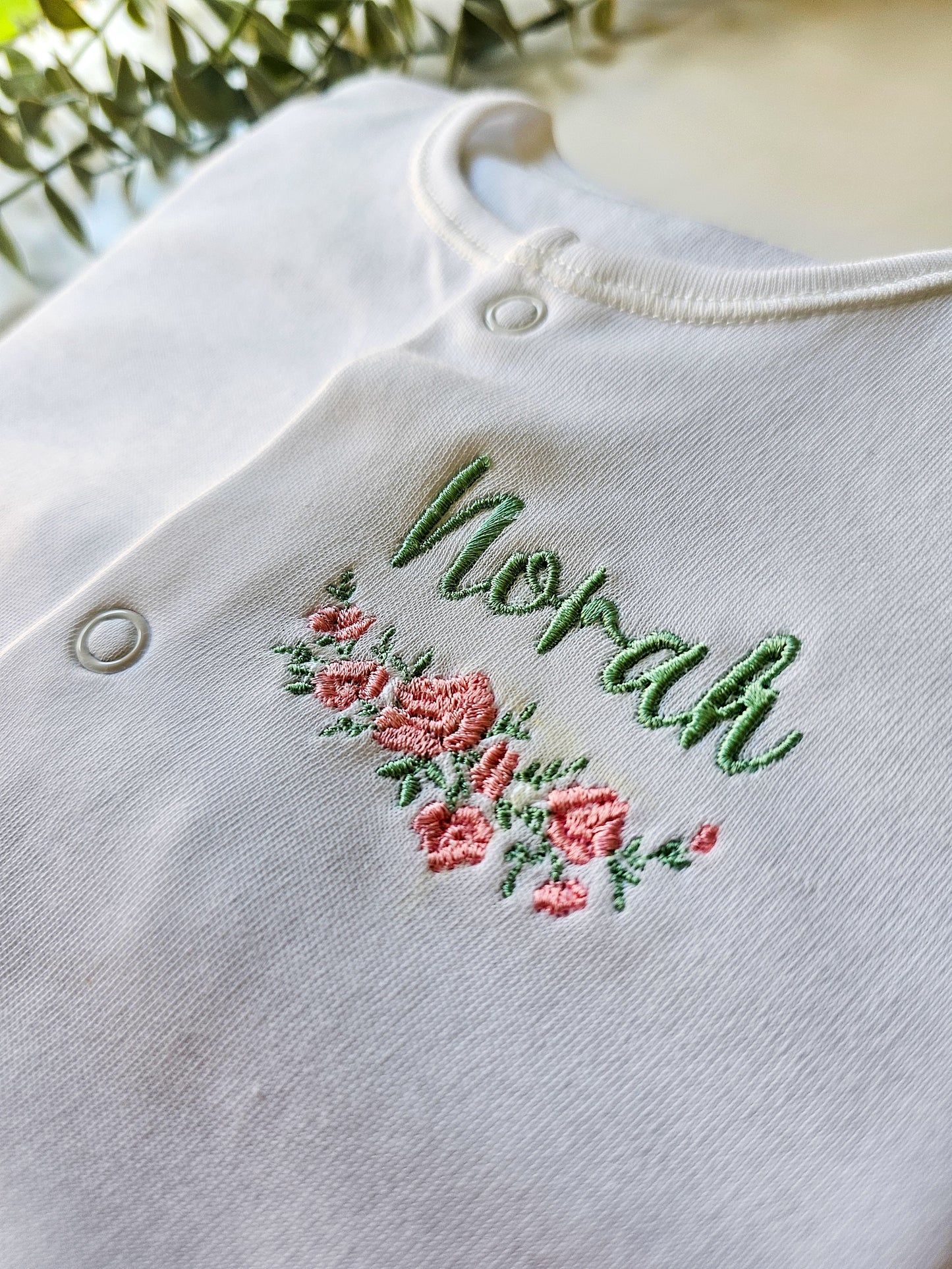 Delicate embroidery, pink and green floral design underneath personalised baby's name in green.
