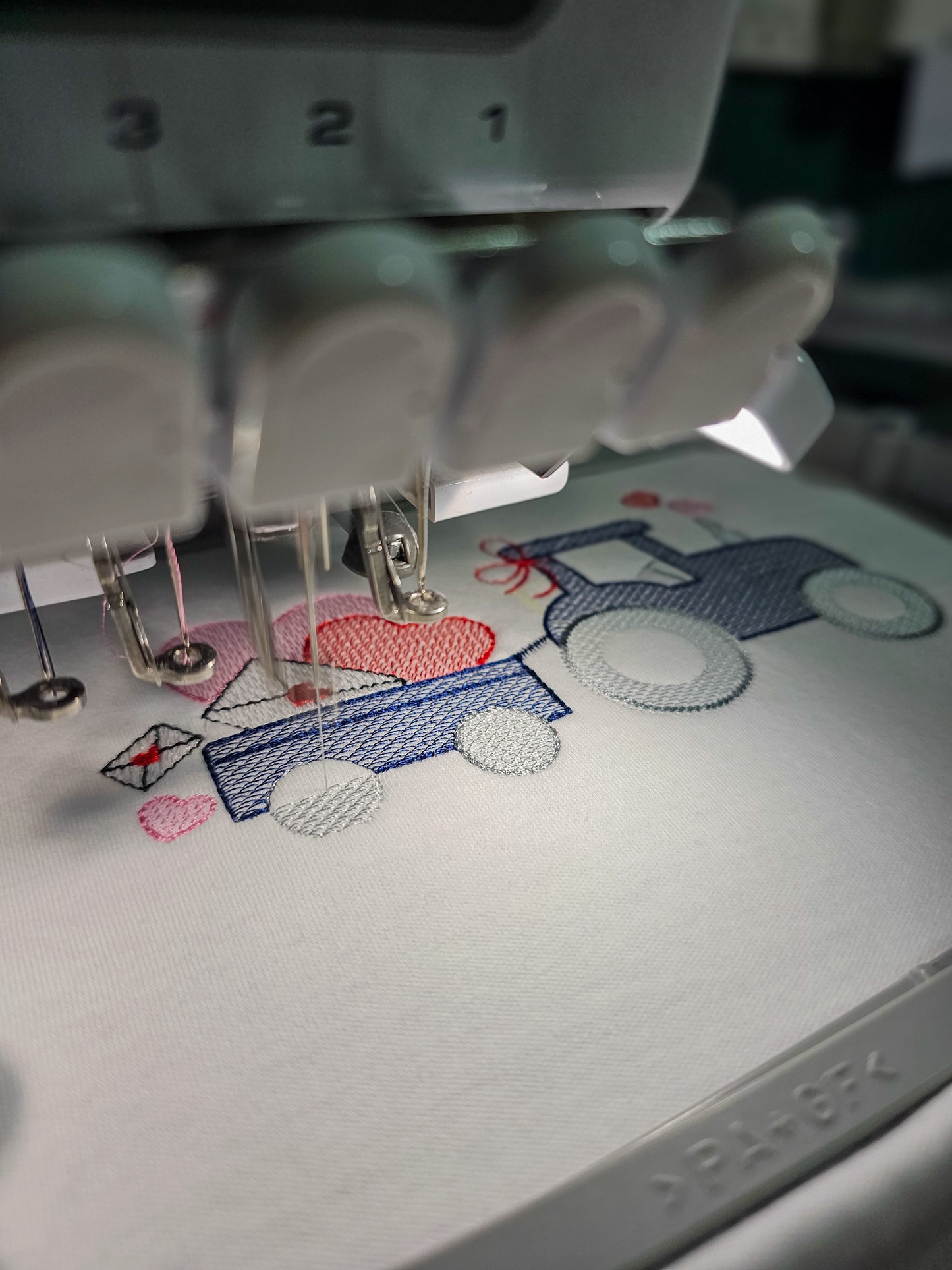 Embroidery machine needle in action with a partially completed design on fabric.
