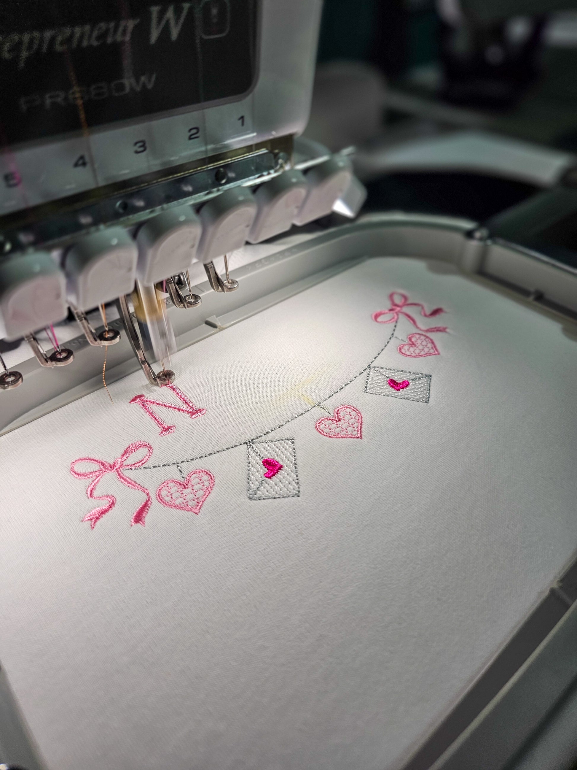 Embroidery machine stitching out personalized embroidery heart designs on a white tshirt