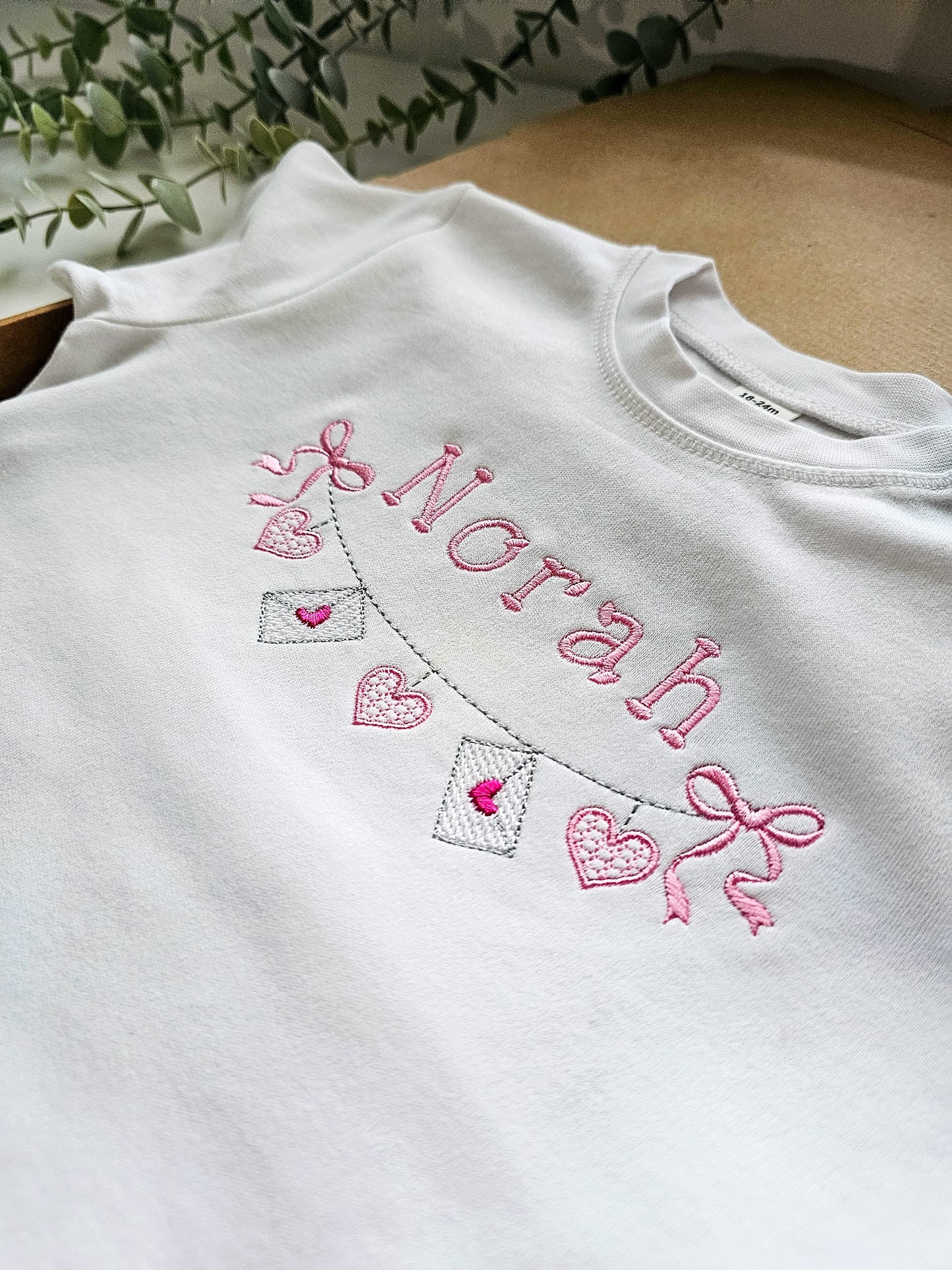 White tshirt with pink embroidery of 'Norah' and decorative valentine elements 