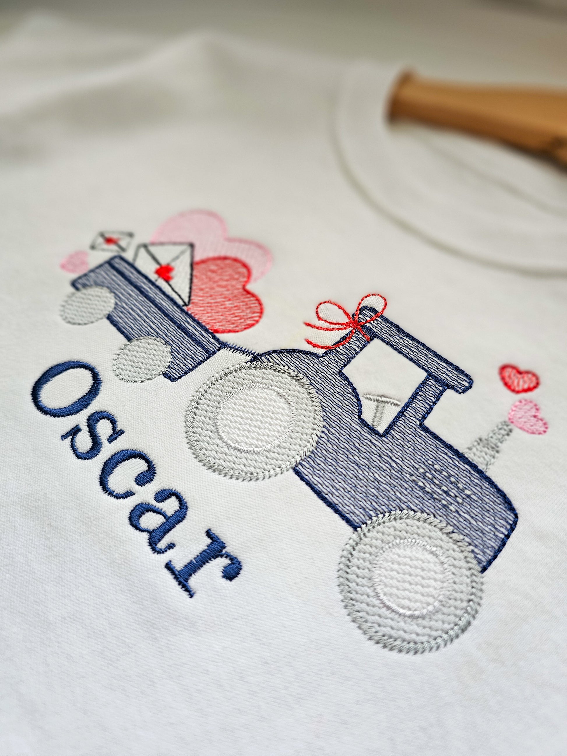 Embroidered design on a white shirt with a blue tractor, pink hearts, and the name 'Oscar'.