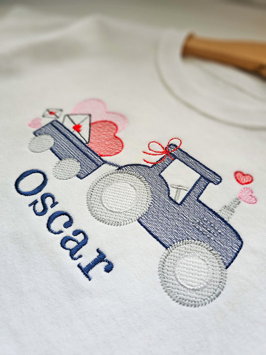 Embroidered design on a white shirt with a blue tractor, pink hearts, and the name 'Oscar'.
