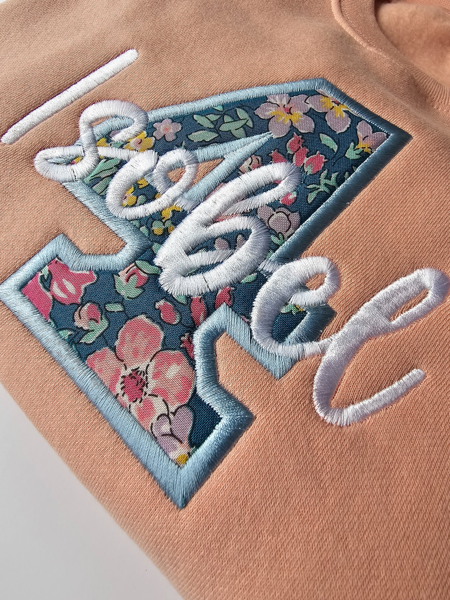 Close up of kids personalized birthday jumper, embroidered with liberty print number 4 and child's name in white thread and curly font.