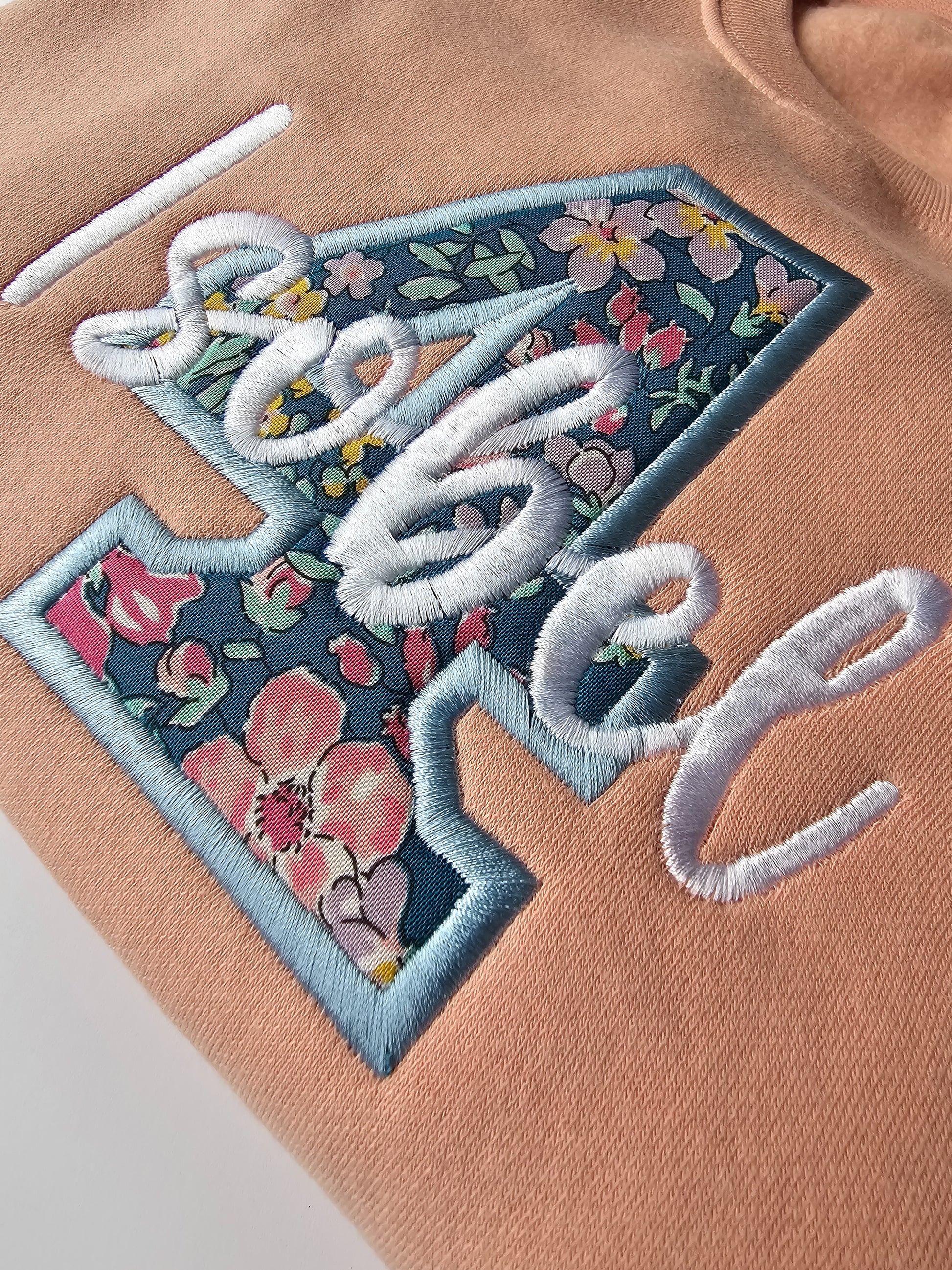 Close up of kids personalized birthday jumper, embroidered with liberty print number 4 and child's name in white thread and curly font.