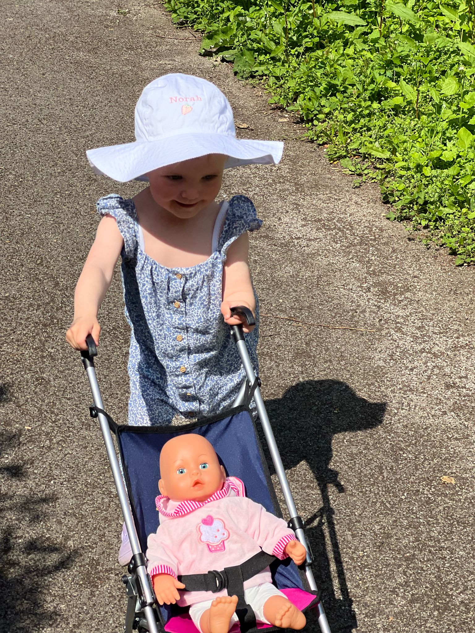 Little girl wearing white wide brimmed sun hat personalised with name and cute pink strawberry design embroidered on the front.