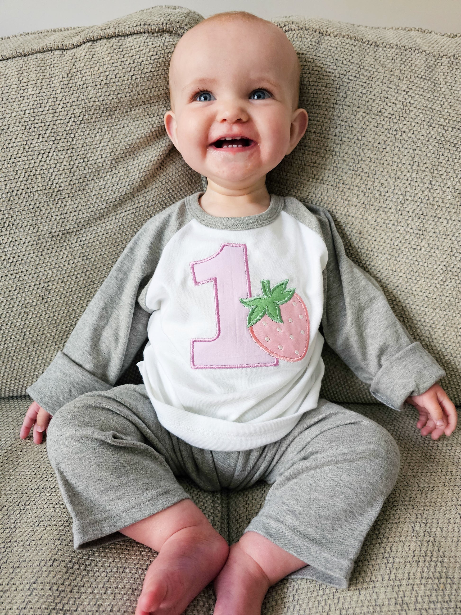Baby wearing strawberry themed first birthday grey pjamas.