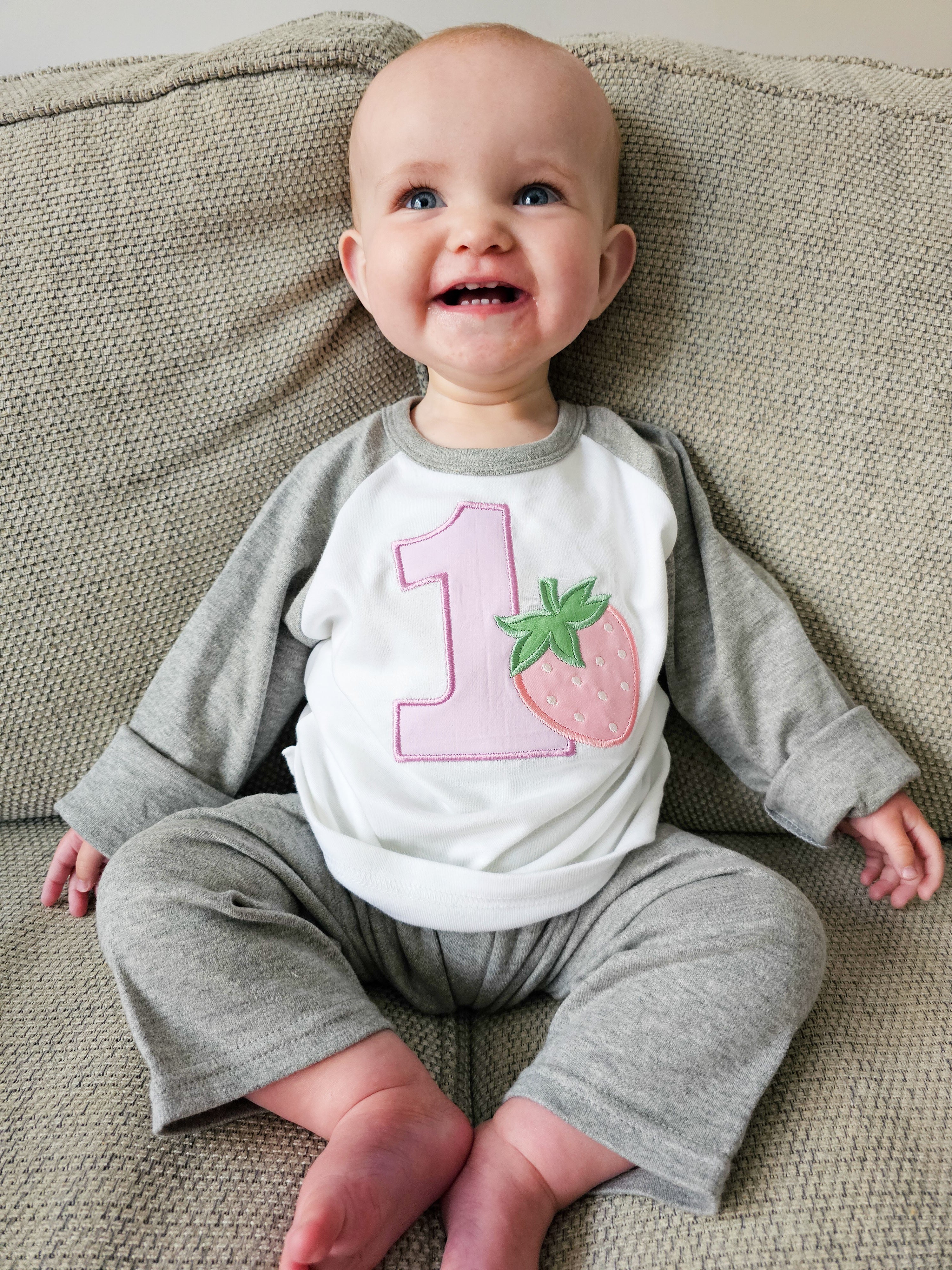 Baby wearing strawberry themed first birthday grey pjamas.