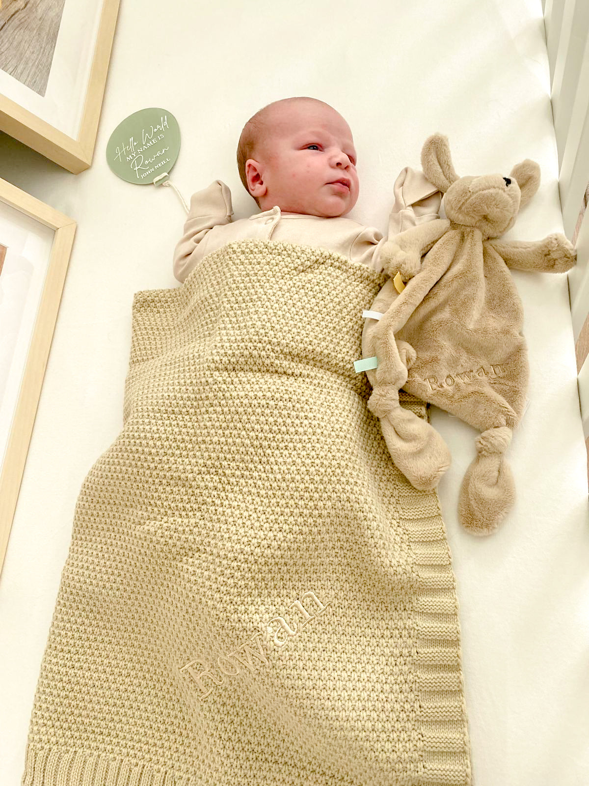 Baby covered in Beige knitted baby blanket personalised with baby's name, embroidered in the same colour thread.