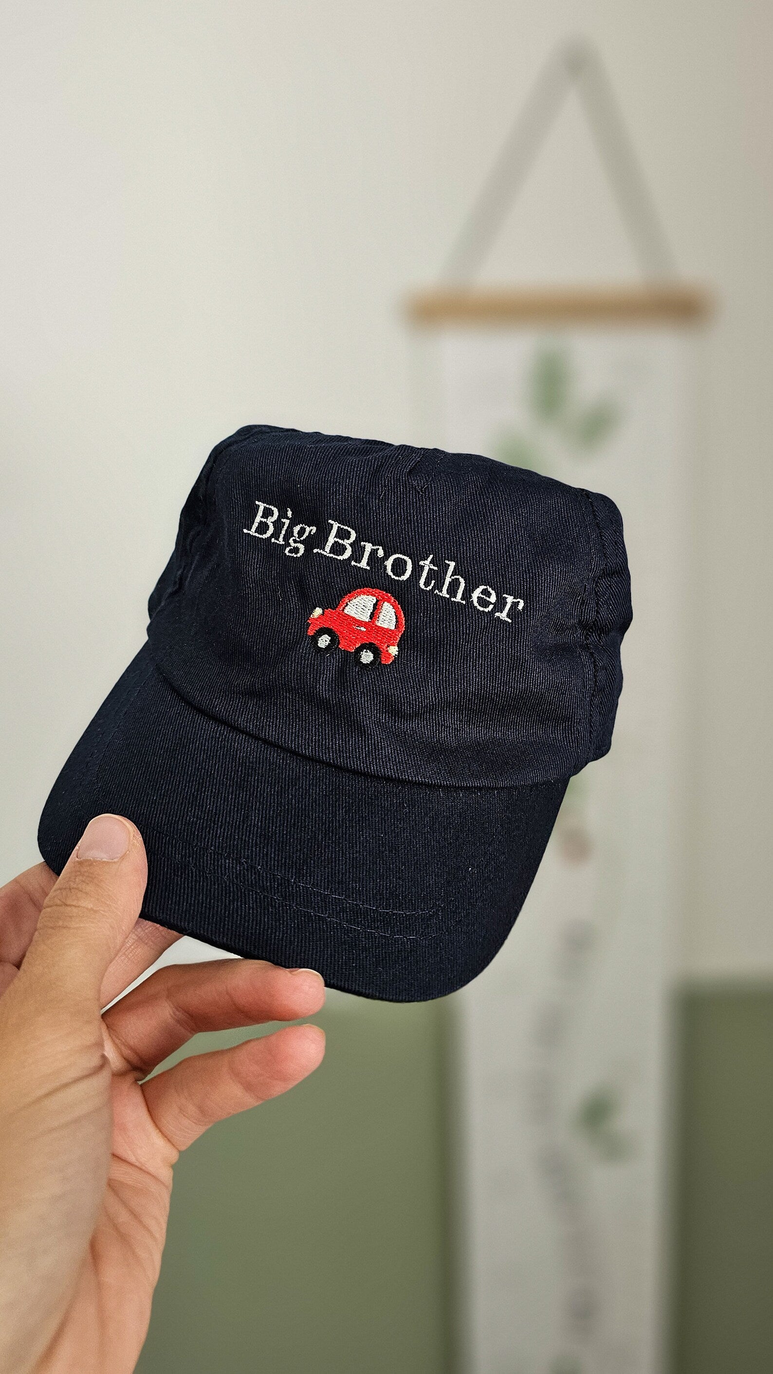 Navy blue cap embroidered with 'Big Brother' and car design held by a hand against a neutral background personalised