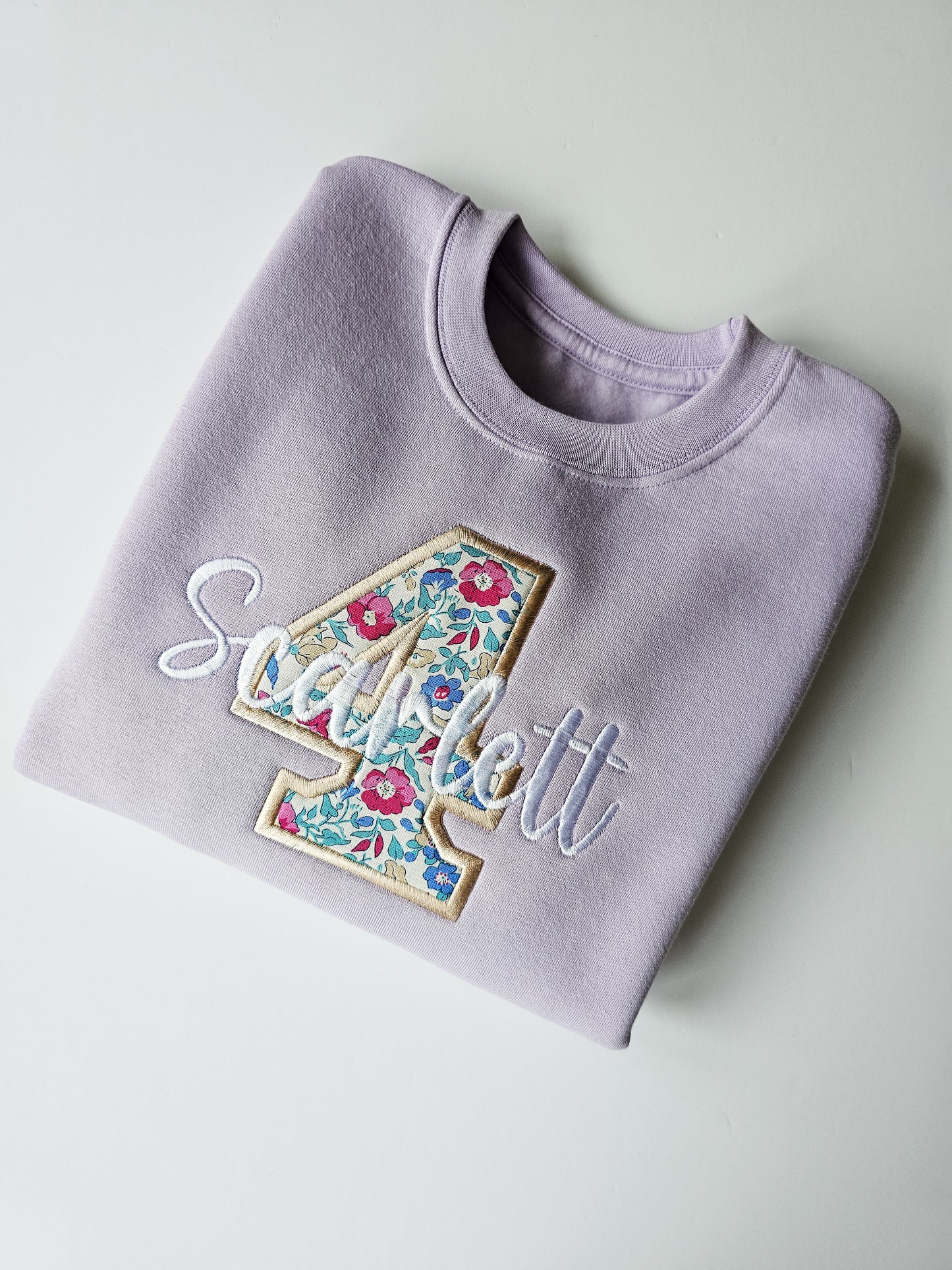 A purple crew neck jumper with the name 'Olivia' and the number '4' embroidered on it, set against a white background.