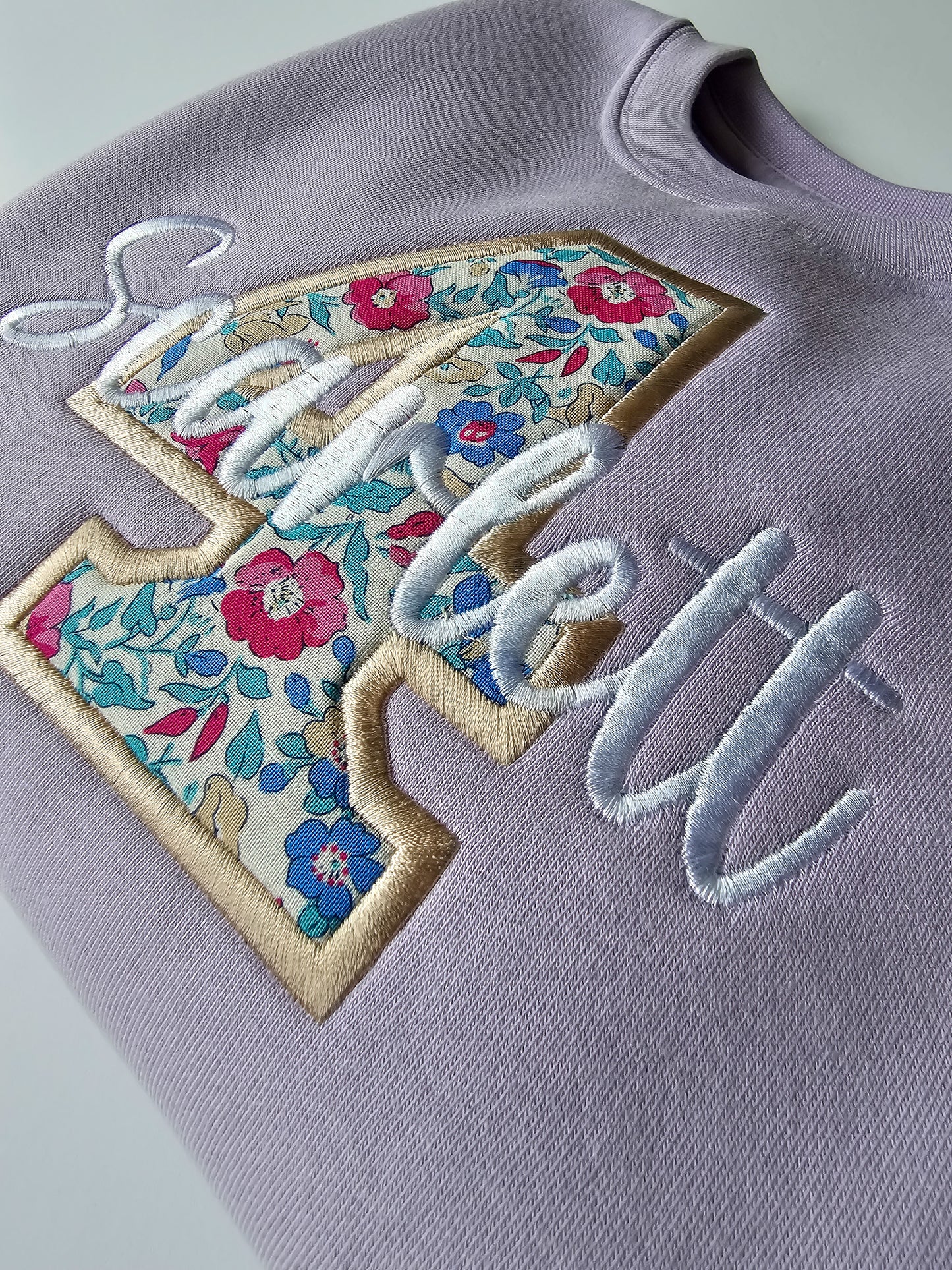 Close up of embroidered 4 birthday jumper, with white and beige stitching