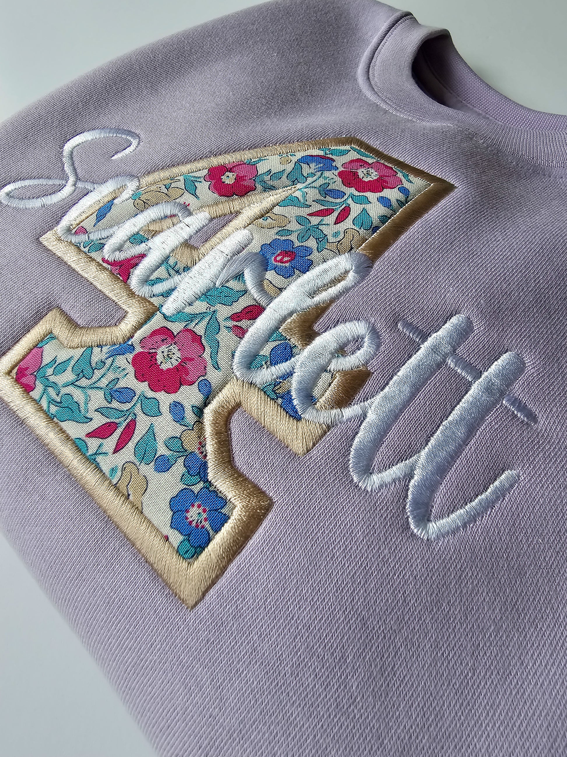 Close up of embroidered 4 birthday jumper, with white and beige stitching