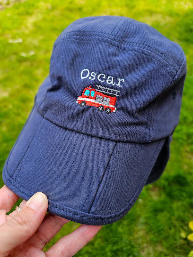 A navy blue children's legionnaires cap embroidered with the name 'Oscar' and an illustration of a red fire engine on the front.