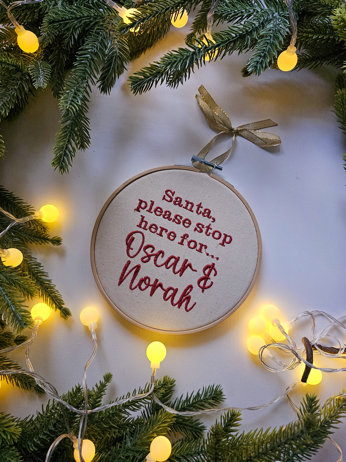 A round embroidery hoop ornament with red embroidered text reading 'Santa, please stop here for.