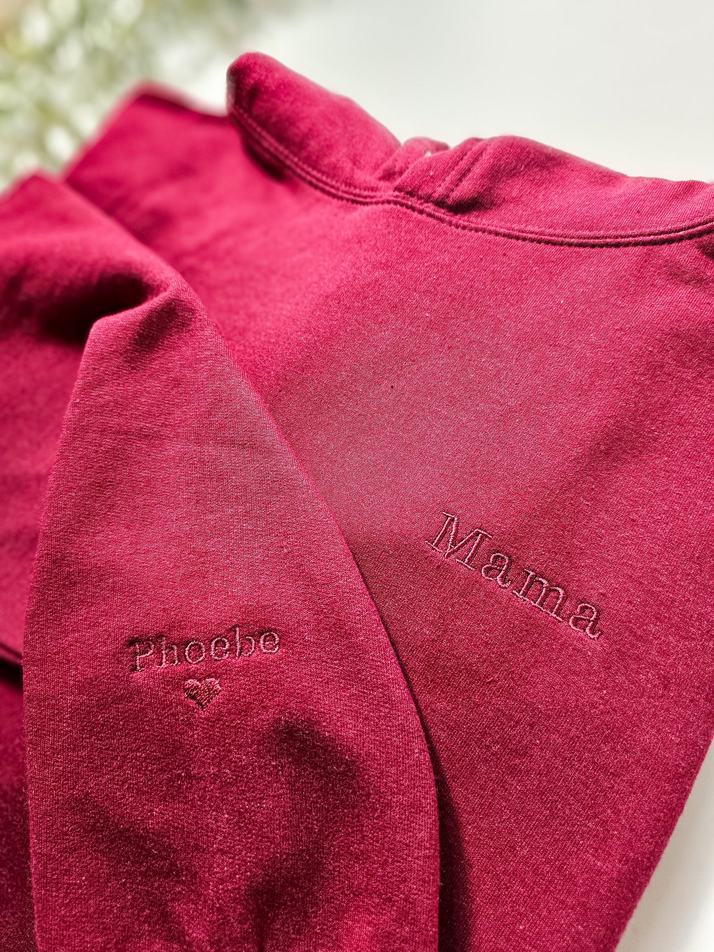 A red personalised embroidered hoodie with the name 'Mama' and a heart symbol on the sleeve, displayed on a white background.