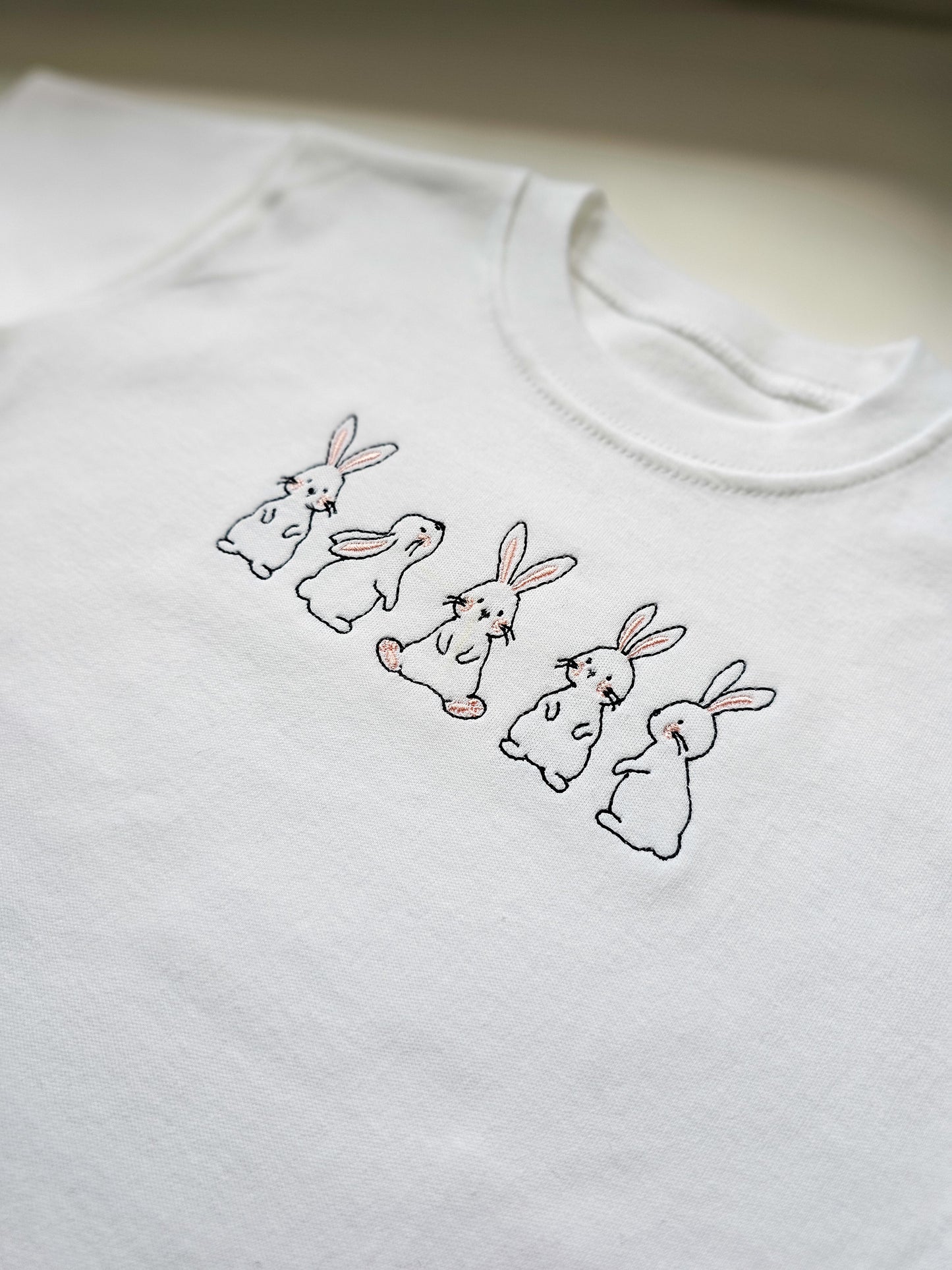White sweatshirt with embroidered bunnies on a plain background