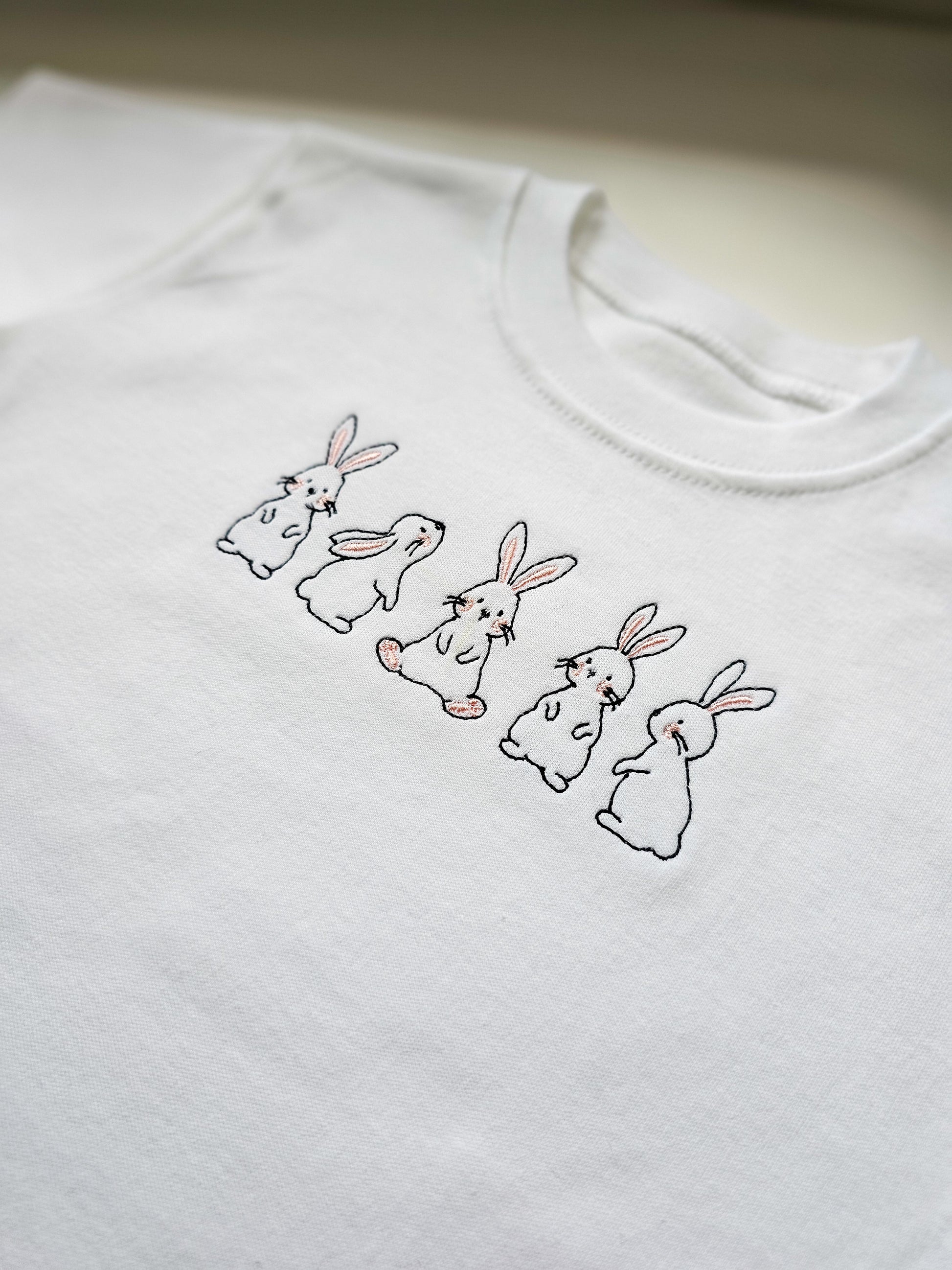 White sweatshirt with embroidered bunnies on a plain background