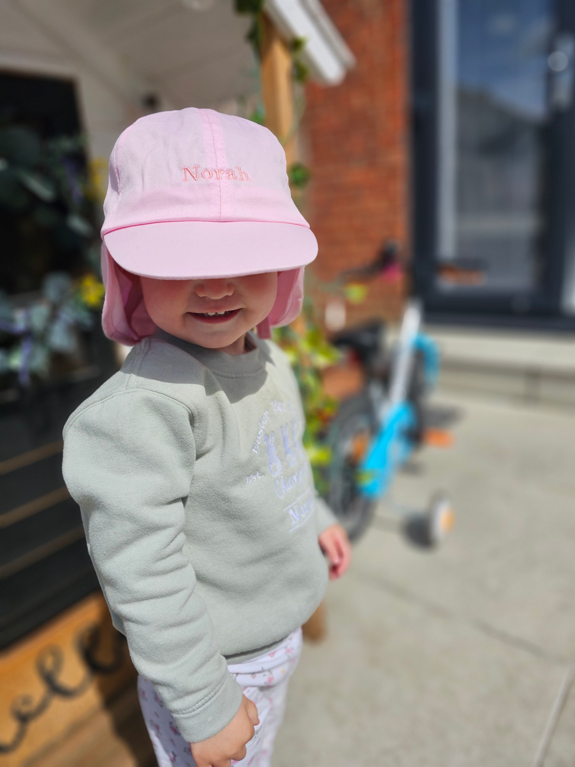 Little girl wearing Pink coloured children/toddler/baby personalised embroidered cap with neck cover.