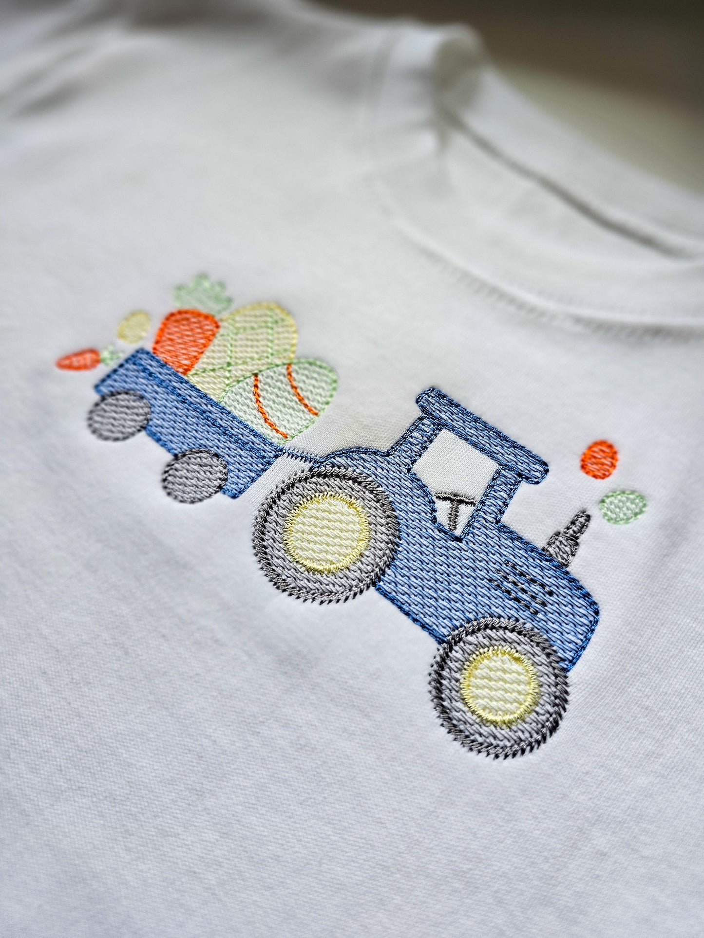 Embroidered blue tractor with easter themed items in the trailer on a white tshirt