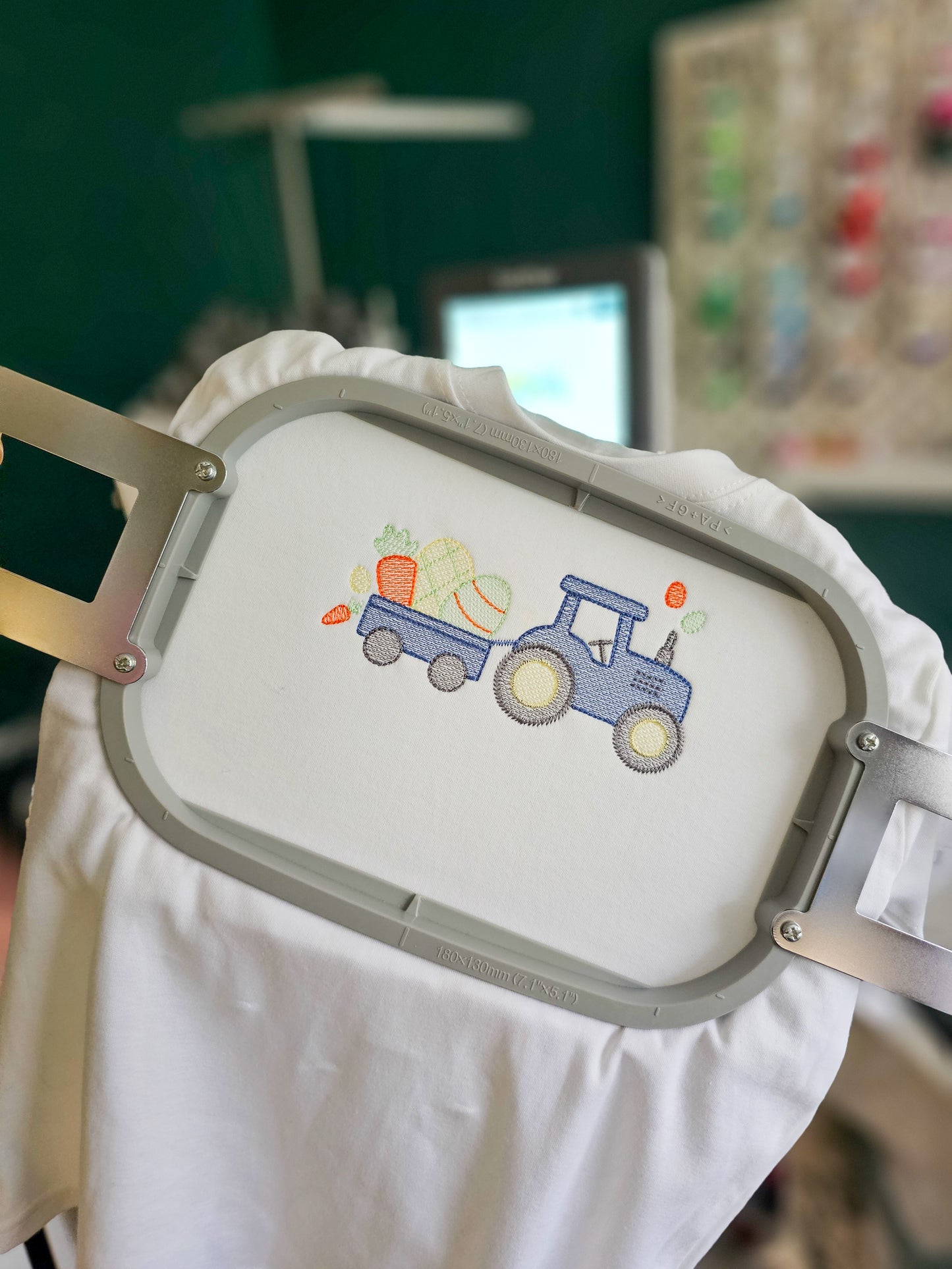 Embroidery hoop with a blue tractor design on a white fabric background.