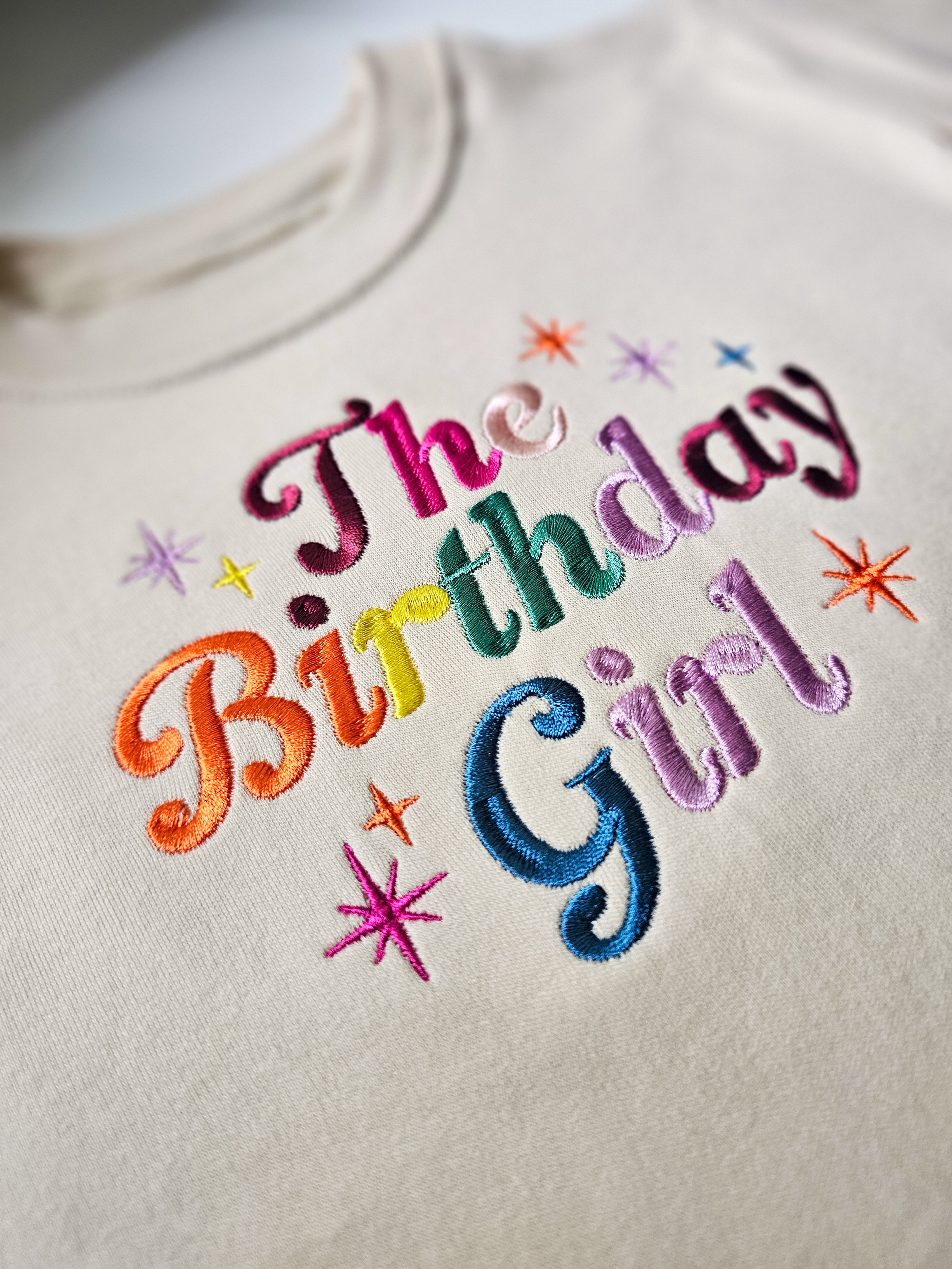 Embroidered text 'The Birthday Girl' on a light background