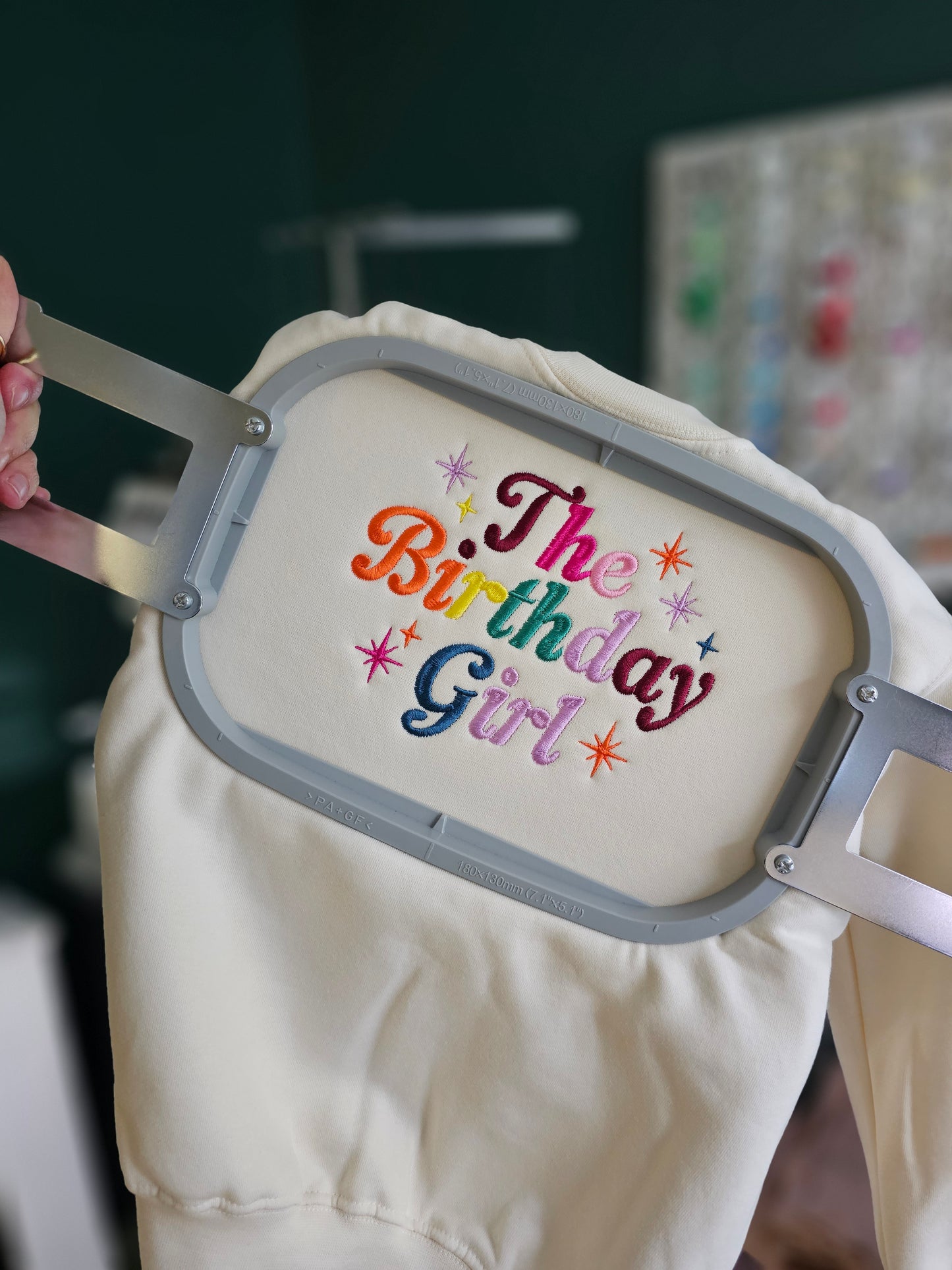 Beige sweatshirt with 'The Birthday Girl' text in colorful letters on an embroidery hoop